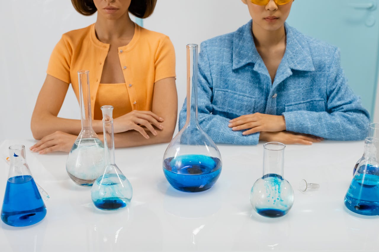 services-01 Two women scientists in a lab with flasks conducting an experiment using blue liquid.
